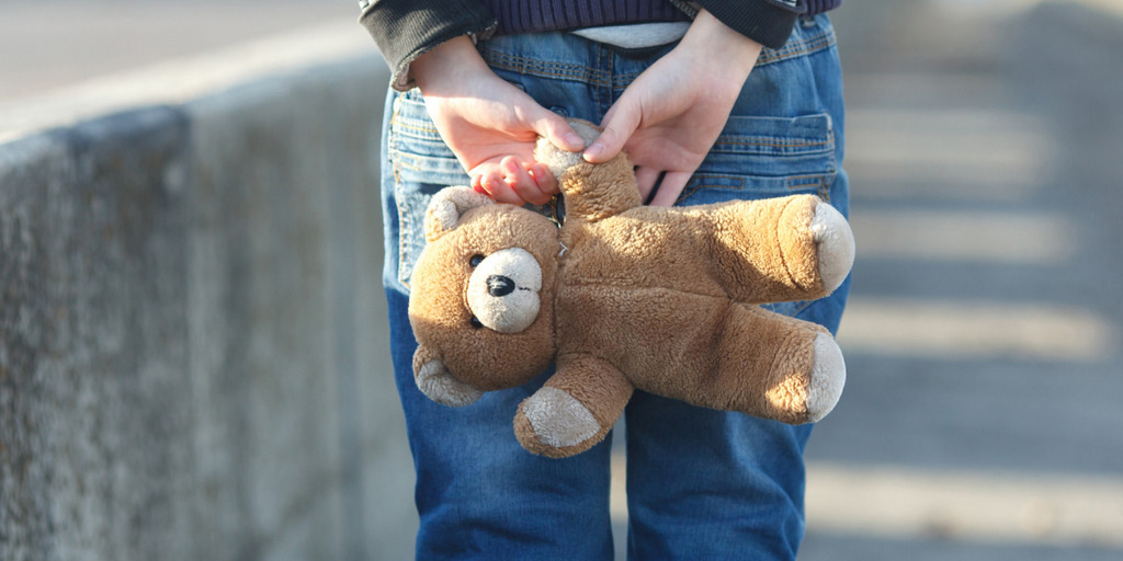 Ausschnitt eines Kinds, das der Kamera den Rücken zudreht und einen Teddybären in den Händen hält.