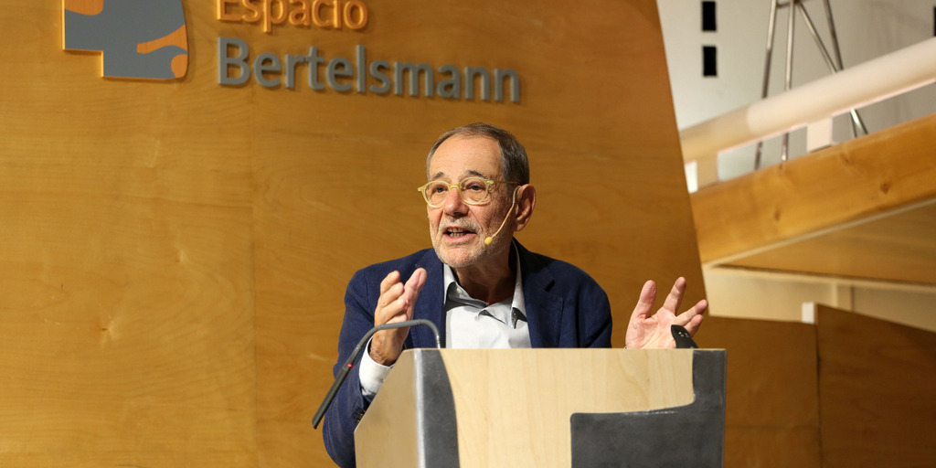 Javier Solana steht hinter einem Rednerpult und hält seinen Vortrag, auf der Wand hinter ihm ist der Schriftzug "Espacio Bertelsmann" zu sehen