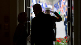 Donald Trump talks to a female staff member in a doorway at the White House while waiting for Egypt's president Al Sisi. Through the opened door, one can see a saluting US soldier and several US flags.