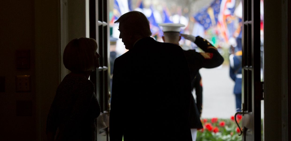 (© Benjamin Applebaum / whitehouse.gov / Wikimedia Commons - Public Domain) Donald Trump talks to a female staff member in a doorway at the White House while waiting for Egypt's president Al Sisi. Through the opened door, one can see a saluting US soldier and several US flags.