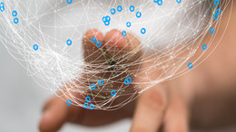Eine Person berührt mit zwei Fingern eine Computergrafik, die einen aus verbundenen Linien und Punkten bestehenden Ball oder Globus darstellt. Die Grafik steht stellvertretend für ein Netzwerk.