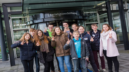Die "Alle Kids sind VIPs"-Kinder Jury 2016 steht vor dem Eingang der Bertelsmann-Stiftung und zeigt das Peacezeichen. Es ist eine Gruppe von 11 Jugendlichen, die aus Jungen und Mädchen besteht.