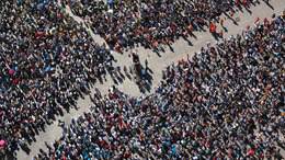 Eine Menschenmasse hat sich auf einem Platz rund um ein großes Rednerpult versammelt. Die Menschenmasse ist in Vogelperspektive zu sehen.