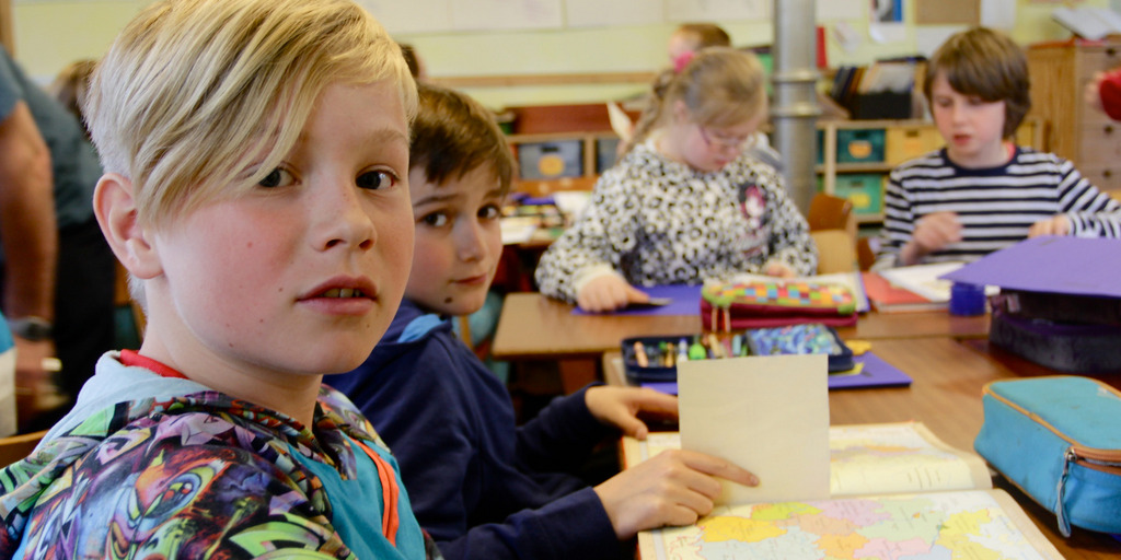 Schulkinder sitzen im Klassenraum und bearbeiten eine Schulaufgabe.