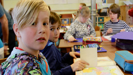 Schulkinder sitzen im Klassenraum und bearbeiten eine Schulaufgabe.