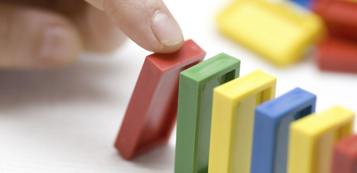 (© wakila / iStockphoto) eine Hand bringt einen Dominostein zu Kippen