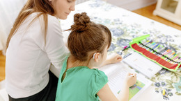 Mutter hilft Tochter, die Hörgeräte trägt, bei den Hausaufgaben.