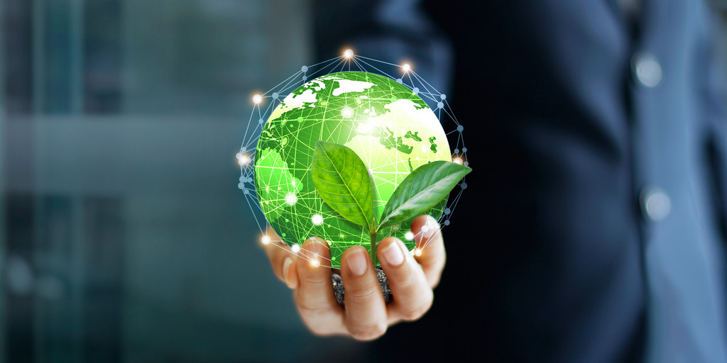 A man dressed in a suit is holding a small version of the globe in his hand, it is colored green. Dots and lines connecting the continents symbolize digital connections. A leaf in front of the globe is symbolizing the environment.