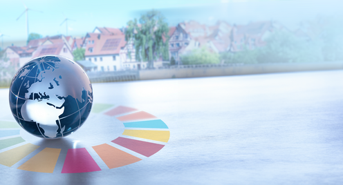 Eine Glaskugel steht auf einem Tisch. Um die Kugel ist der SDG-Kranz sichtbar. Im Hintergrund sieht man eine Stadt mit Windrädern und Solaranlagen auf den Dächern.