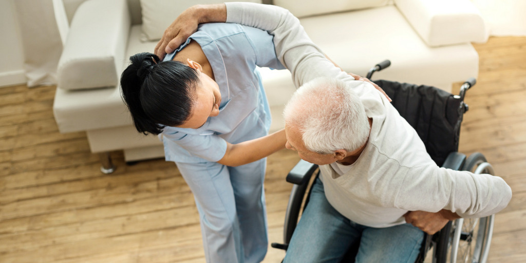 Eine weibliche Pflegekraft hilft einem alten Mann, aus dem Rollstuhl aufzustehen