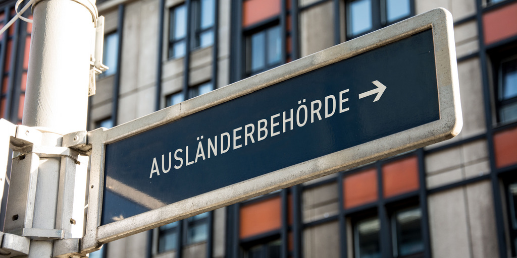 Im Hintergrund ist ein Gebäude zu sehen, im Vordergrund ein Schild mit der Aufschrift "Ausländerbehörde"