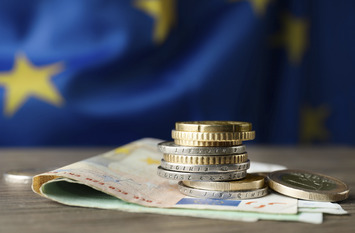 Coins and banknotes on wooden table against European Union flag.