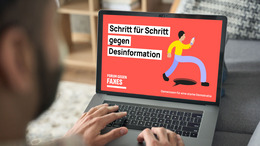 Ein Mann tippt auf der Tastatur seines Laptops, auf dem ein Bild mit dem Logo des "Forum gegen Fakes" sowie dem Text "Schritt für Schritt gegen Desinformation" zu sehen ist.