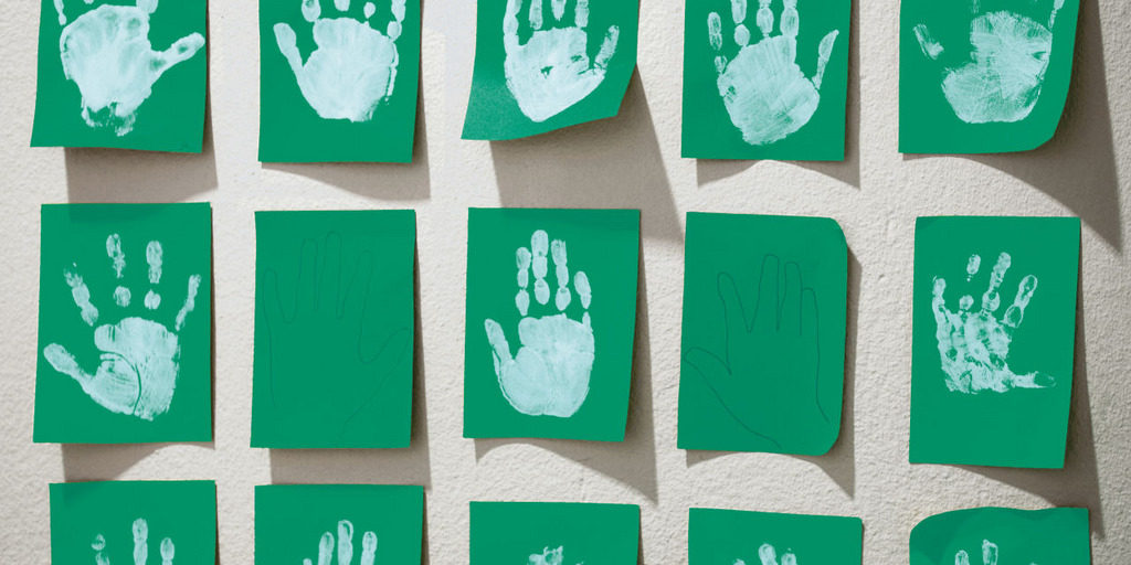 An der Wand einer Kita hängen grüne Blätter Papier, auf denen Kinder in weißer Farbe ihre Handabdrücke hinterlassen haben.