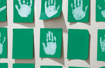 Weiße Handabdrücke auf grünem Papier nebeneinander gereiht.