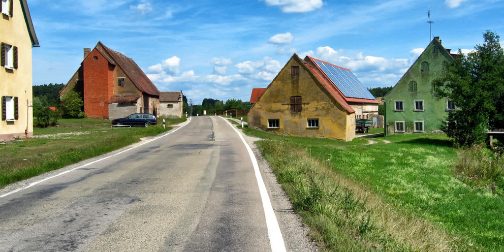 Eine verlassene Straße im ländlichen Bayern mit heruntergekommenen Häusern.