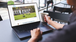 Eine Person sitzt an einem Tisch mit einer Tasse. Vor ihr steht ein Laptop. Auf dem Bildschirm des Laptops ist der Blog Nachhaltige Kommunen zu sehen.