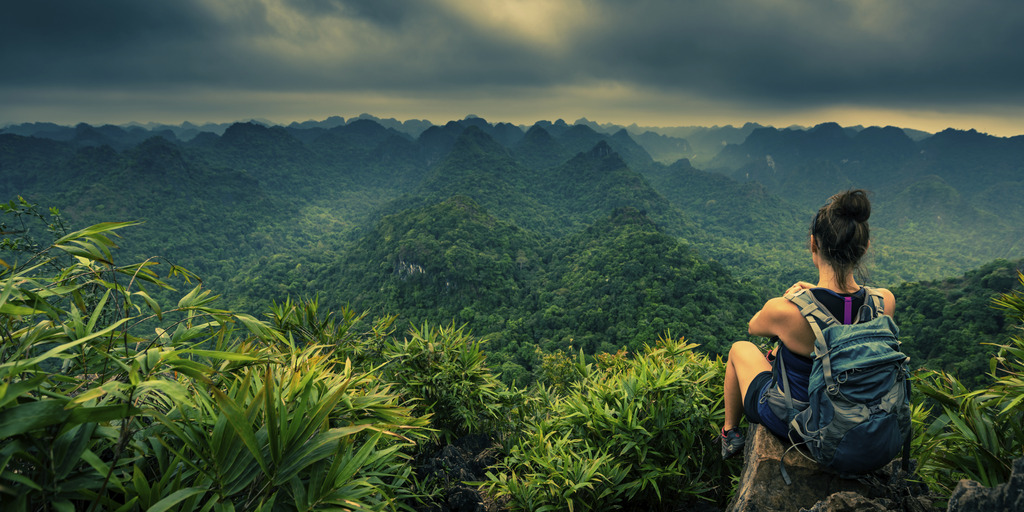 Blick von oben in den Dschungel einer Frau, die an der Bergkante sitzt