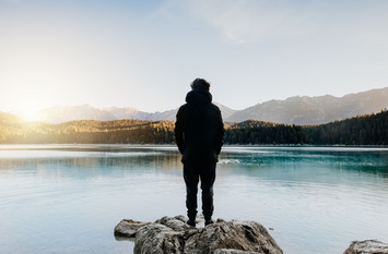 Mensch von hinten schaut auf wunderschönen See bei Sonnenaufgang.