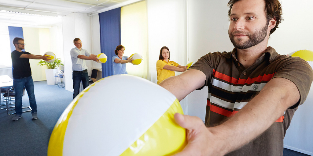 Mehrere Menschen bilden einen Halbkreis und vollziehen mit Wasserbällen in den Händen eine Fitnessübung.