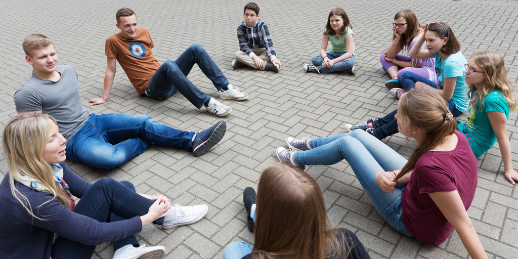 [Translate to English:] Kinder und Jugendliche sitzen im Kreis auf dem Boden