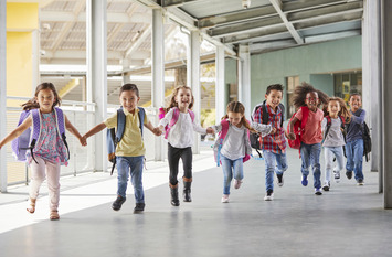 Grundschulkinder rennen händchenhaltend durch den Korridor.