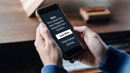 [Translate to English:] Twi white hands holding a smart phone. On the Screen it says "Alert. This content has been flagged by independent fact-checkres. Proceed with caution before sharing."
