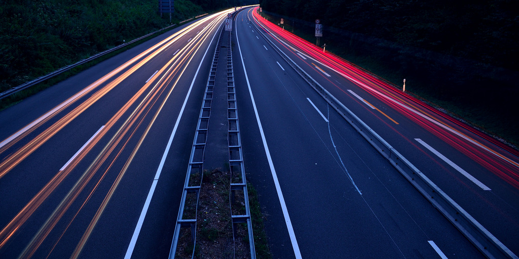 [Translate to English:] Zeitrafferaufnahmen von einer Autobahnbrücke auf die Autobahn. Es ist dunkel. Zu sehen sind nur die Scheinwerfer in langen rot und gelben Linien.