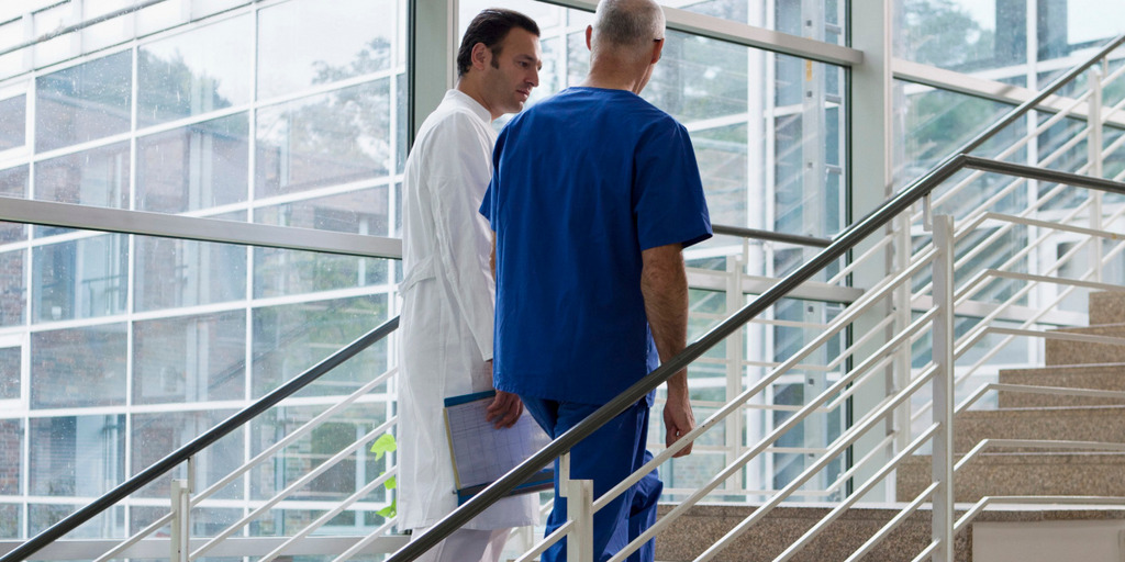 Ein Arzt und ein Krankenpfleger gehen eine Treppe in einem Krankenhaus hinauf und unterhalten sich.