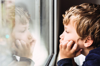 Ein Junge steht vor einem Fenster. Er stützt die Ellenbogen auf und hält mit den Händen seinen Kopf.