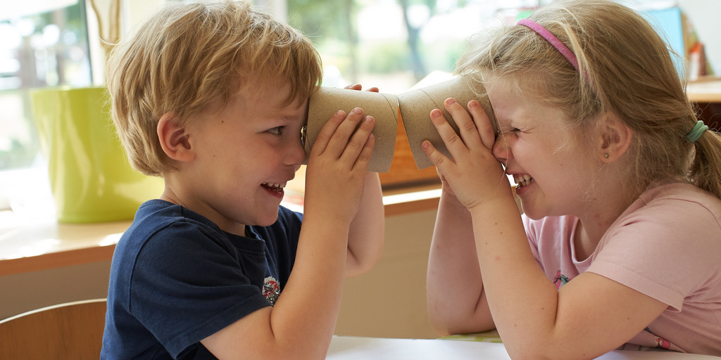 Zwei Kinder sehen sich durch eine Papprolle an.