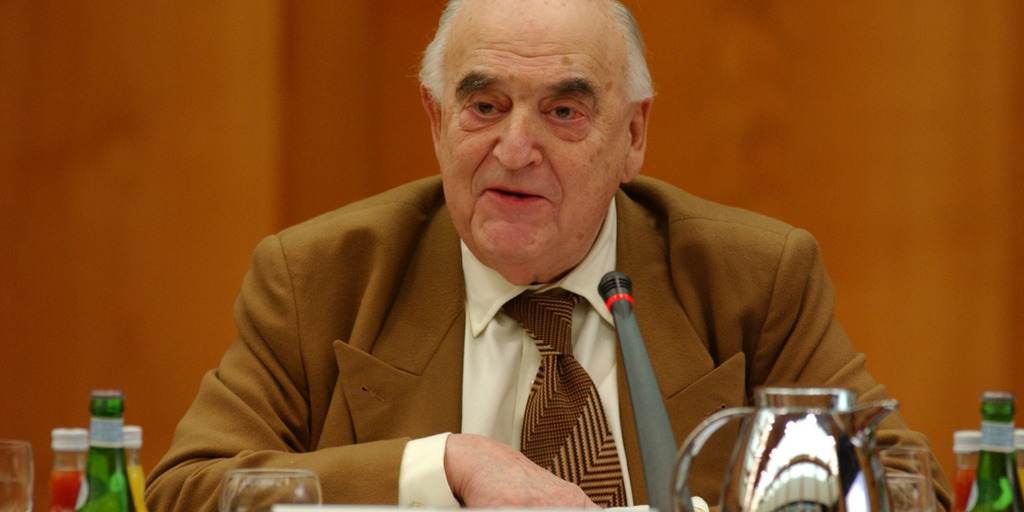 Archivaufnahme von Lord Weidenfeld beim International Bertelsmann Forum 2004 in Berlin. Er sitzt lächelnd an einem Tisch, vor ihm steht ein Mikrofon.