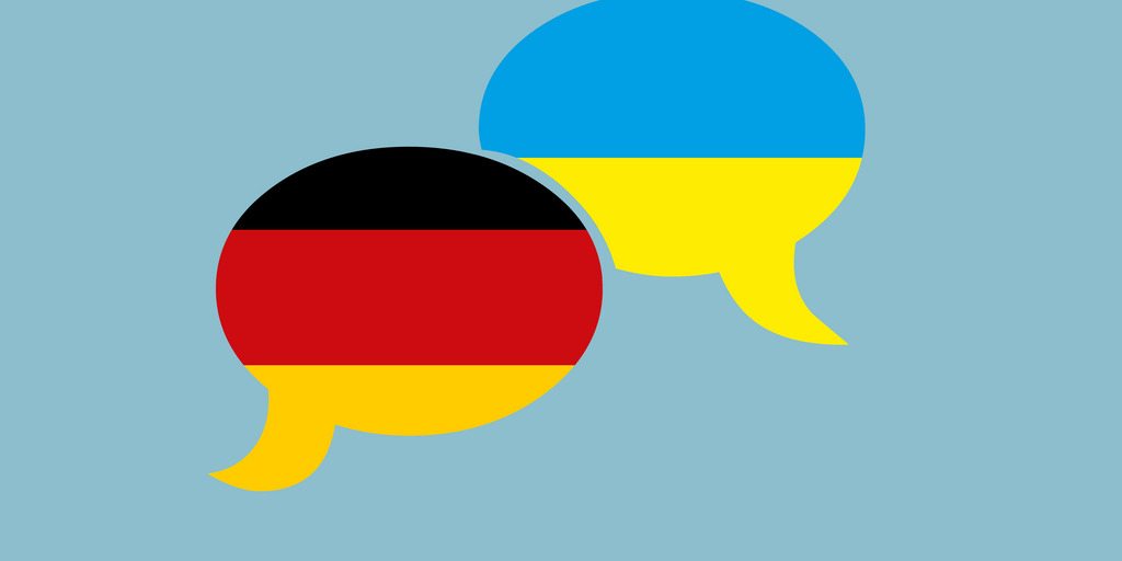 Zwei Sprechblasen nebeneinander. Eine hat die Farben der deutschen und die andere Sprechblase die Farben der ukrainischen Flagge