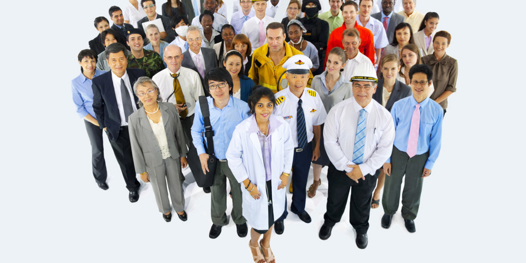 A group of people in working dress, including a doctor, a pilot, a firefighter, business people and construction engineers. They are standing closely together in a large group and smile into the camera.