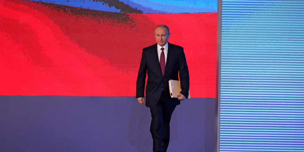 Mit einer Dokumentenmappe unter dem Arm betritt Russlands Präsident Wladimir Putin eine Bühne, hinter der auf einem riesigen Bildschirm eine russische Flagge projiziert wird.