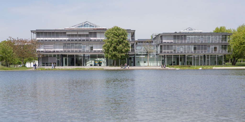 Das Gebäude der Bertelsmann Stiftung an einem sonnigen Tag, im Vordergrund ist der See vor dem Stiftungsgebäude zu sehen.