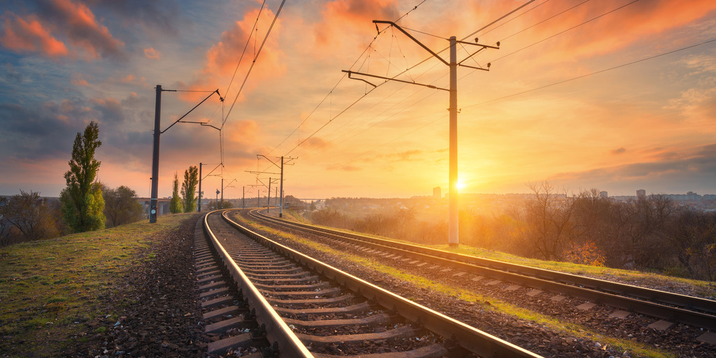 Bahnhof vor wunderschönem Himmel bei Sonnenuntergang. Industrielandschaft mit Eisenbahn, farbenfrohem blauem Himmel mit roten Wolken, Sonne, Bäumen und grünem Gras. Eisenbahnknotenpunkt. Schwerindustrie. Abend im Herbst.