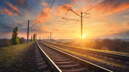 Bahnhof vor wunderschönem Himmel bei Sonnenuntergang. Industrielandschaft mit Eisenbahn, farbenfrohem blauem Himmel mit roten Wolken, Sonne, Bäumen und grünem Gras. Eisenbahnknotenpunkt. Schwerindustrie. Abend im Herbst.