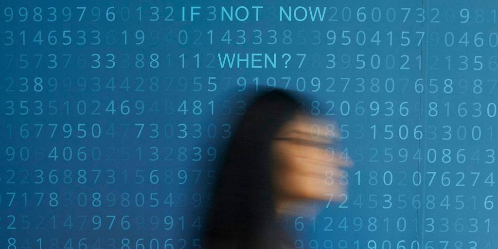Motion blur of a woman in front of the blue background and numerical code on which the lettering “IF NOT NOW WHEN” can be seen.