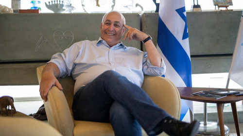 Chemi Peres sits on a couch and smiles.