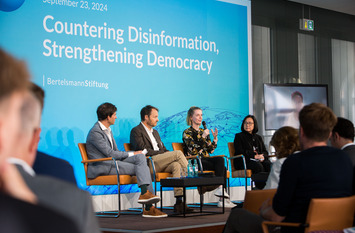 Blick auf die Bühne während der Podiumsdiskussion zum Thema "Democracy in Times of Disinformation". Cathleen Berger von der Bertelsmann Stiftung sitzt auf einem Stuhl und spricht. Neben ihr sitzen der Moderator Dominik Hierlemann von der Bertelsmann Stiftung, Michael Meyer-Resende von Democracy Reporting International und Yvonne Chua von der University of the Philippines und hören Cathleen Berger zu.