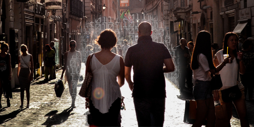 [Translate to English:] Mann und Frau spazieren in einer Gasse umgeben von Touristen