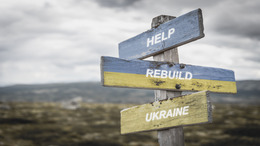 Ein Wegweiser mit drei Schildern: help, rebuild, Ukraine