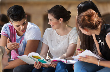 Drei Personen sitzen drau&szlig;en auf dem Schulhof und lernen