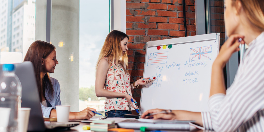 Eine Frau erklärt am Flipchart und zwei andere Frauen hören ihr am Tisch sitzend zu.