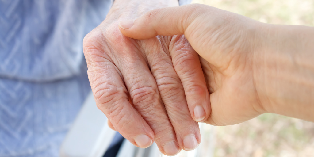 Eine Hand hält die andere Hand eines älteren Menschen, der im Rollstuhl sitzt