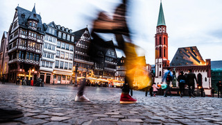 Über das Kopfsteinpflaster einer historischen Altstadt einer deutschen Stadt spazieren verschiedene Passantinnen und Passanten.