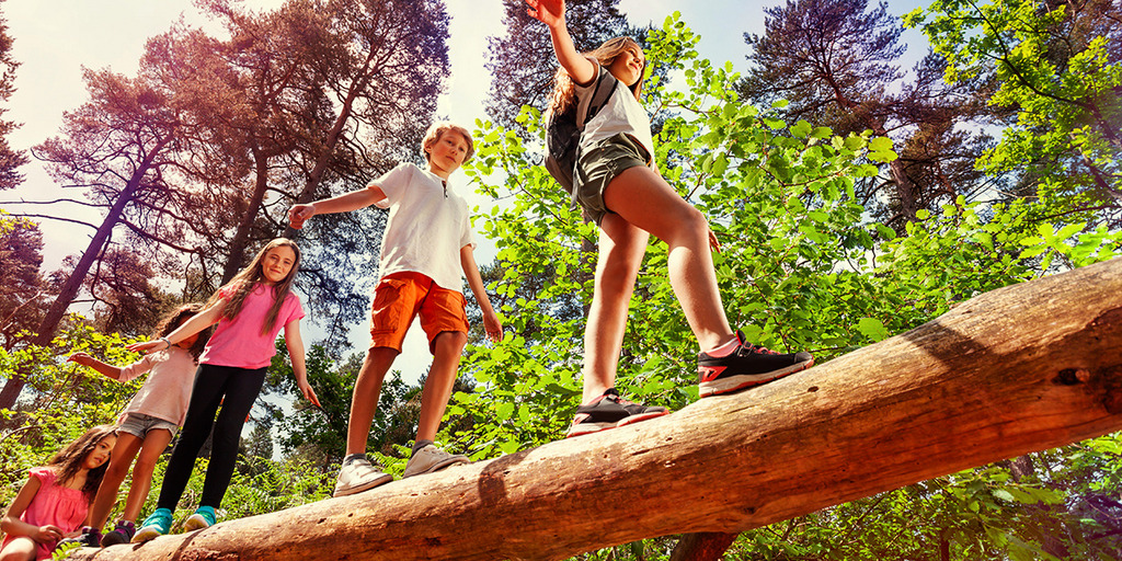 Kinder balancieren auf einem Baumstamm.