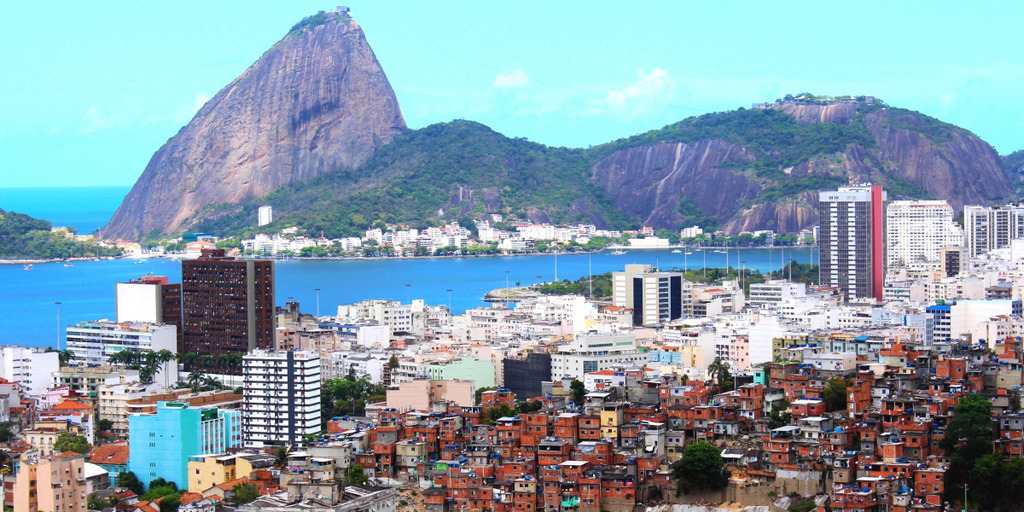 Ein Panorama-Blick auf Rio de Janeiro: Im Hintergrund ist der Zuckerhut zu sehen, im Vordergrund die Häuser der Stadt, unter anderem eine Armensiedlung.