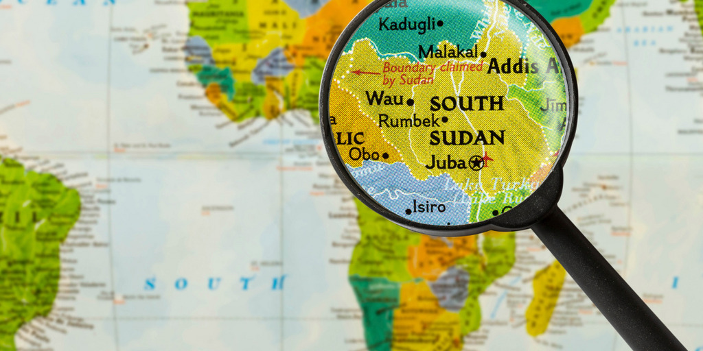 Blick auf eine Karte des afrikanischen Kontinents. Darauf liegt eine Lupe, die die Karte des Südsudan vergrößert.